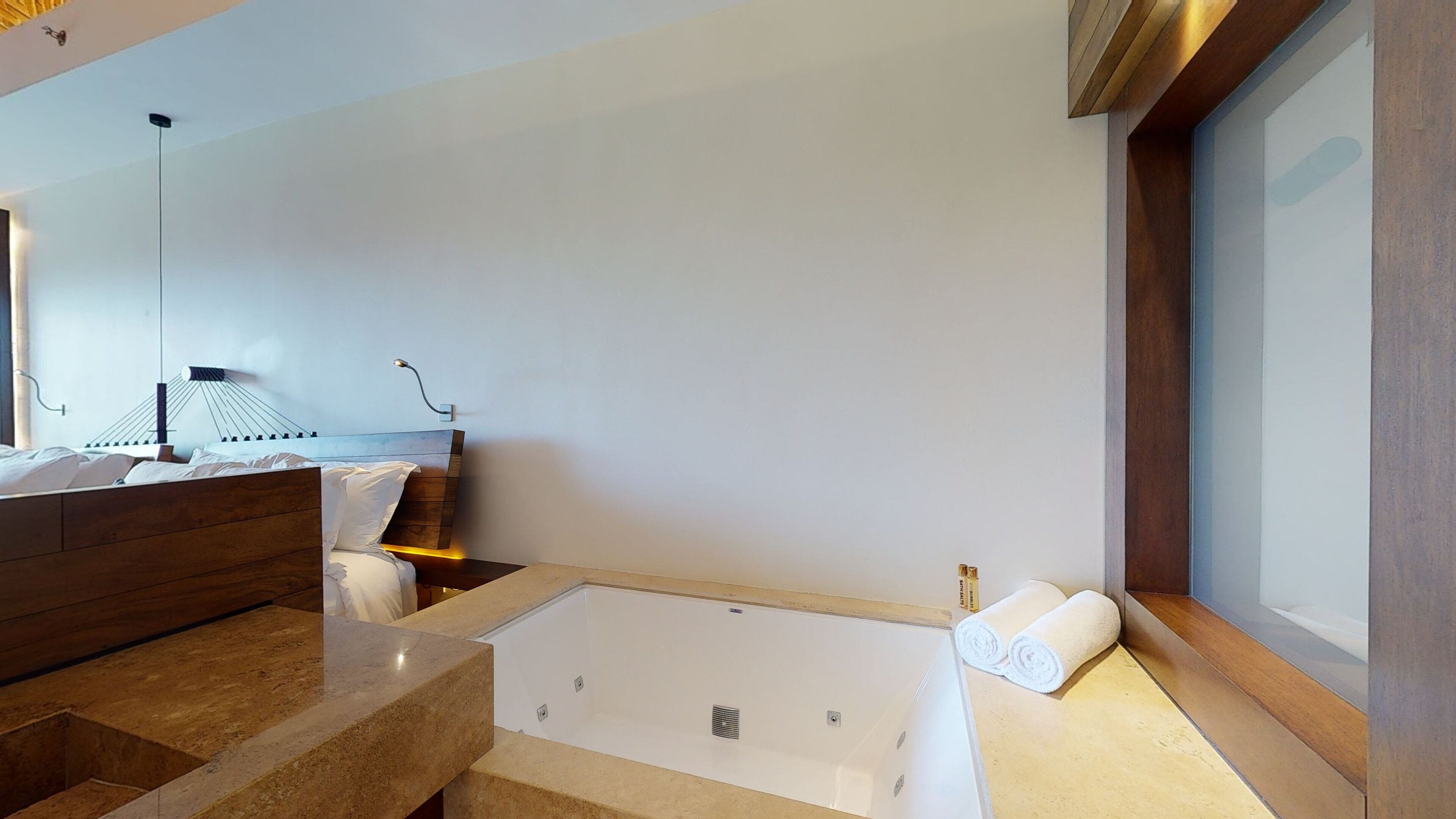 Une salle de bain moderne avec une grande baignoire, un meuble-lavabo en bois et un luminaire fixé au mur.