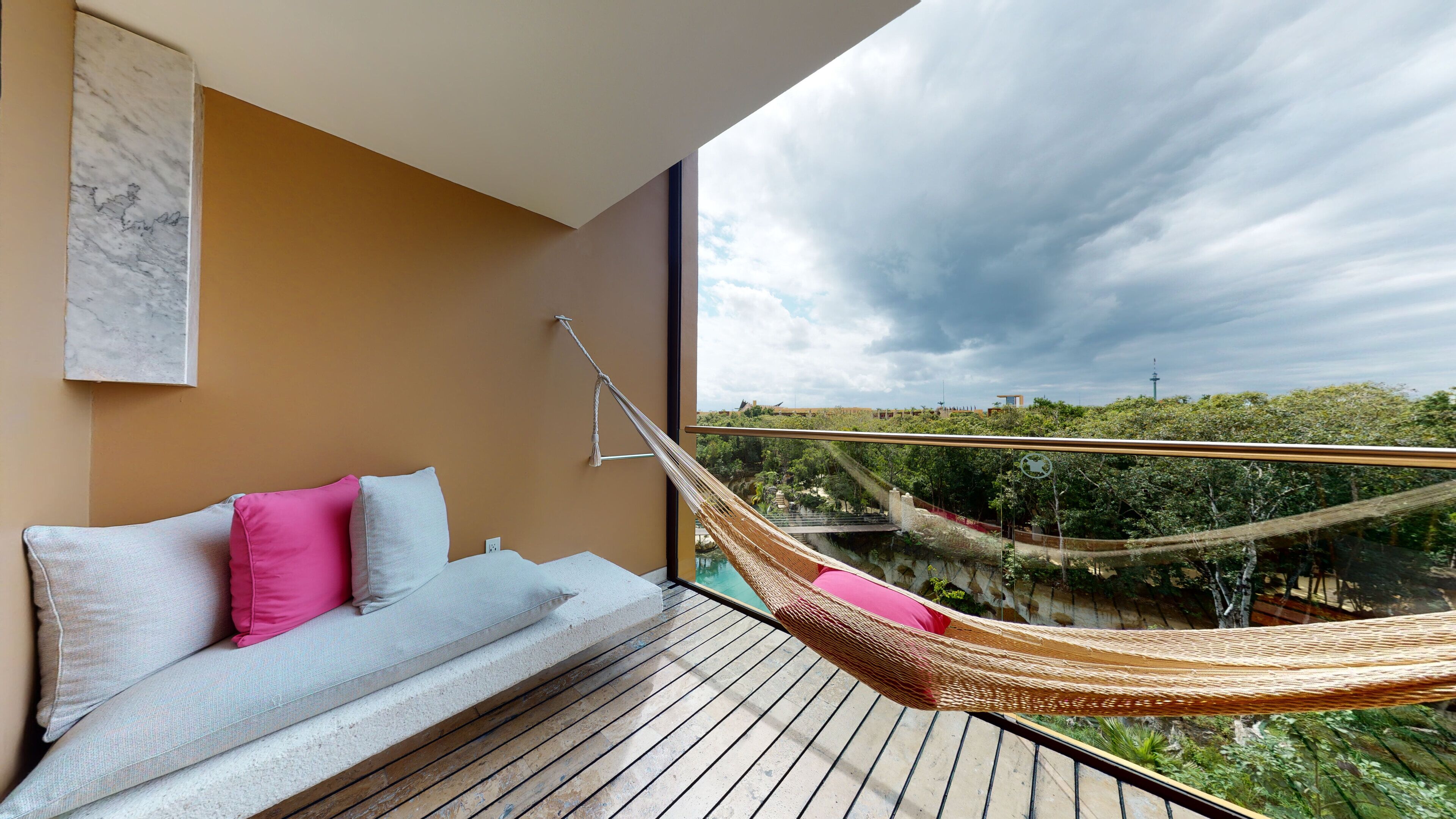 A balcony with a hammock, a sofa with cushions, and a view of a bridge and greenery.