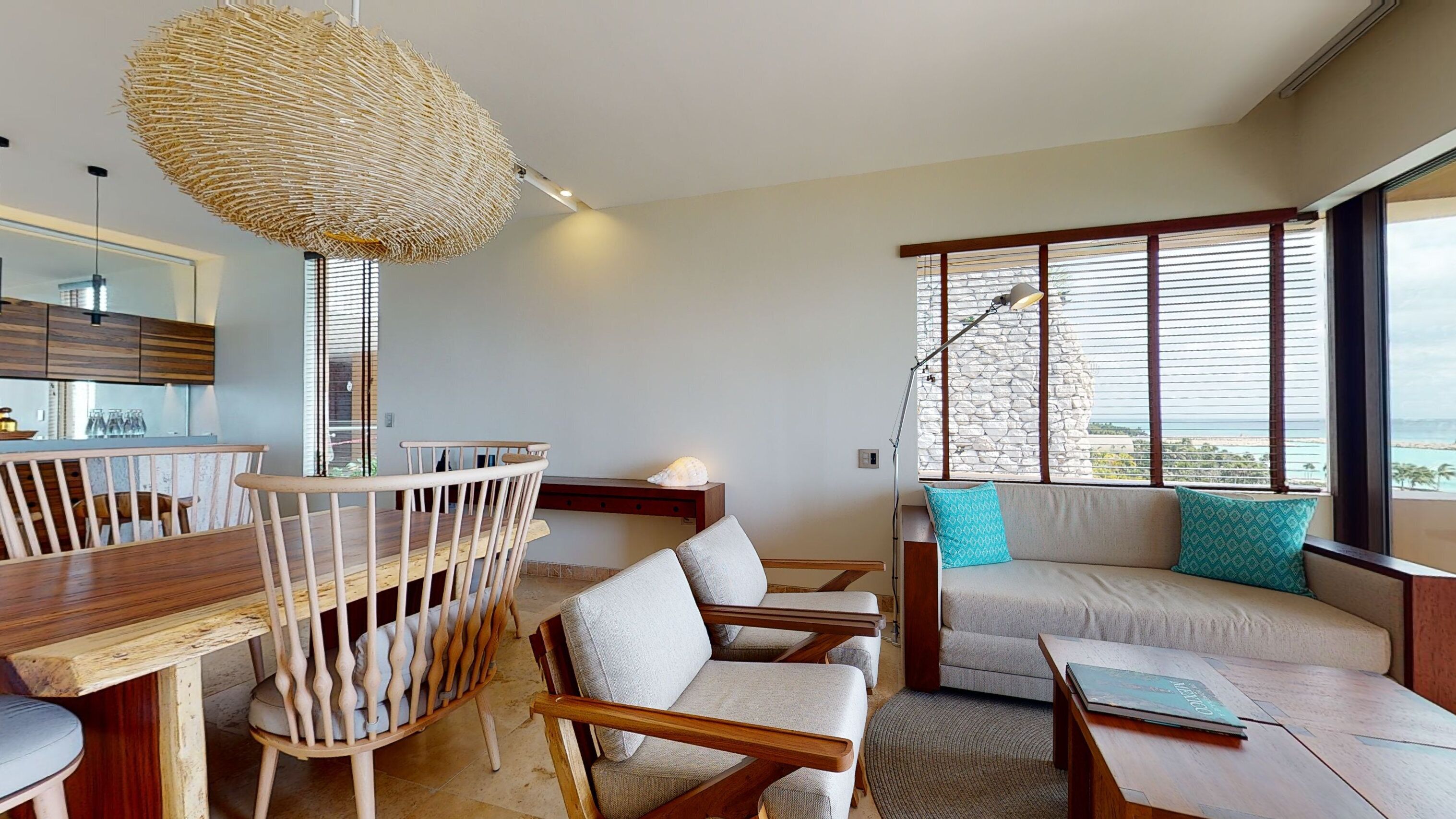 Una sala de estar moderna con una mesa de comedor de madera, sillas, un sofá con cojines estampados y un ventanal con vistas.