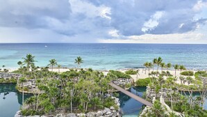 A resort with a beach view, palm trees, and a rocky area with a bridge. - Hotel Xcaret Arte - All Parks / All Fun Inclusive, Adults Only - All inclusive (Playa del Carmen)