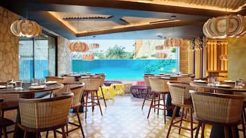 Un restaurant avec des chaises en osier, des tables rondes et des luminaires suspendus.