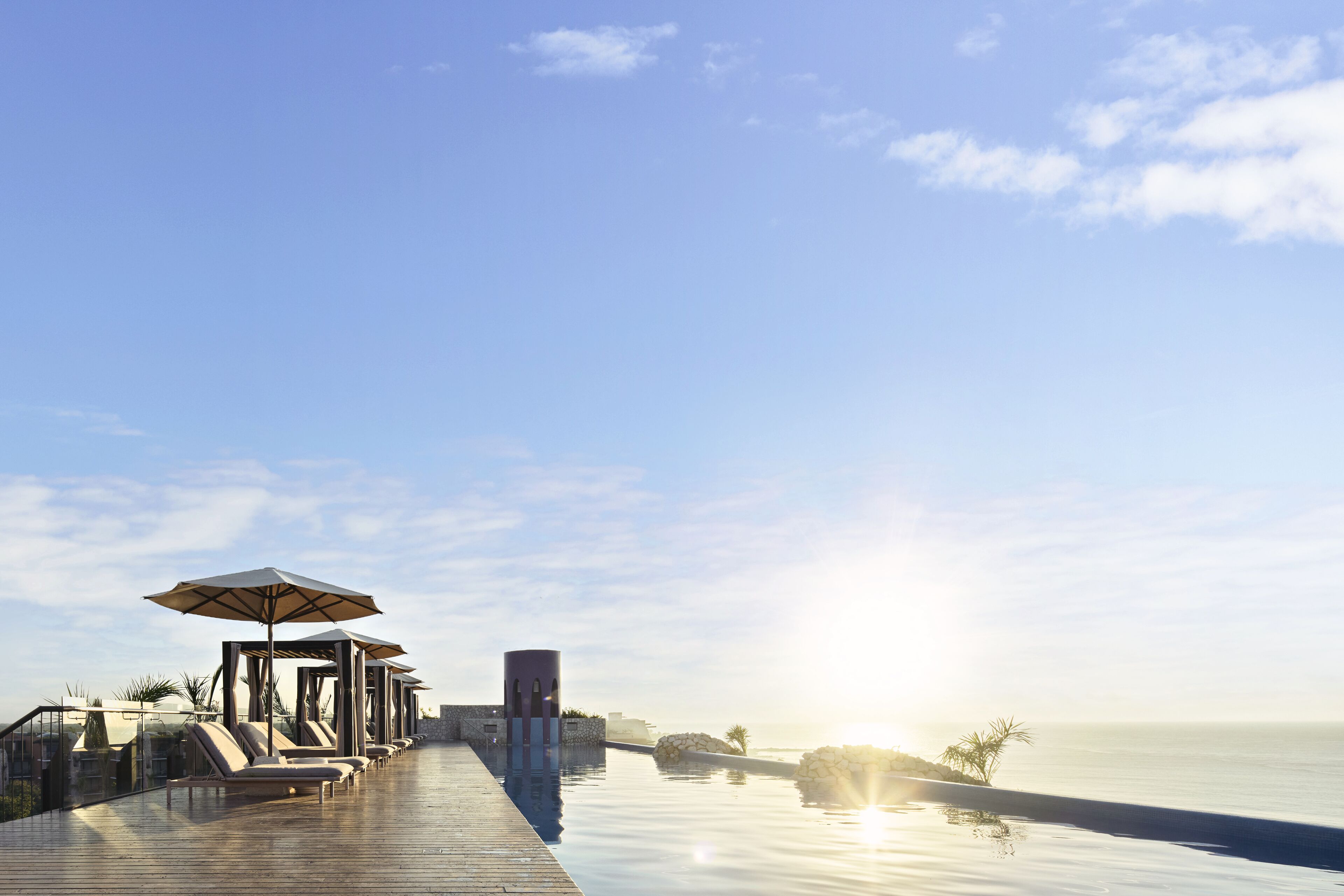 Una piscina infinita tranquila con sillones y sombrillas, con vista al mar en calma.