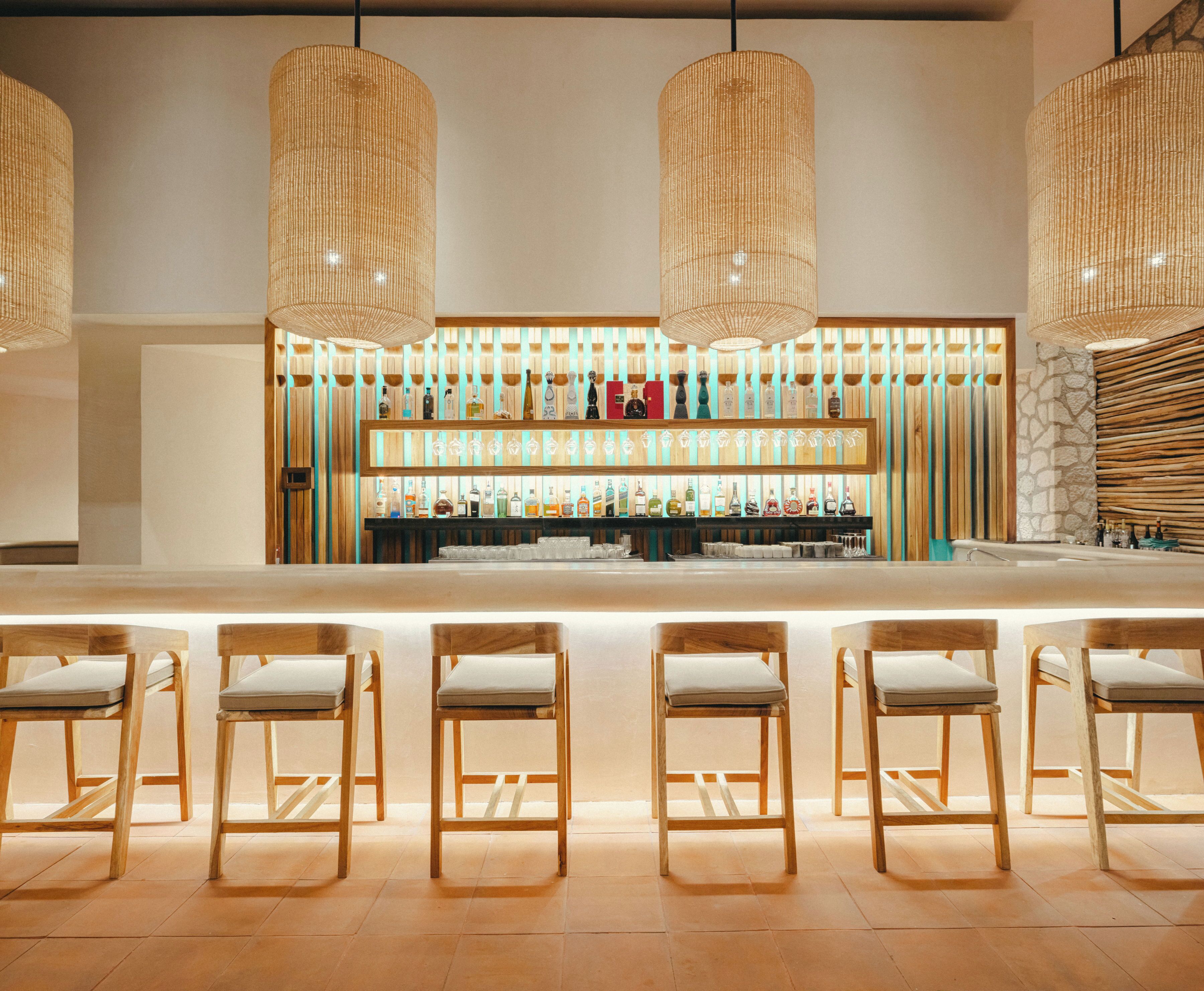 Zona de bar con sillas de madera y una estantería llena de botellas.