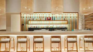 Zona de bar con sillas de madera y una estantería llena de botellas.