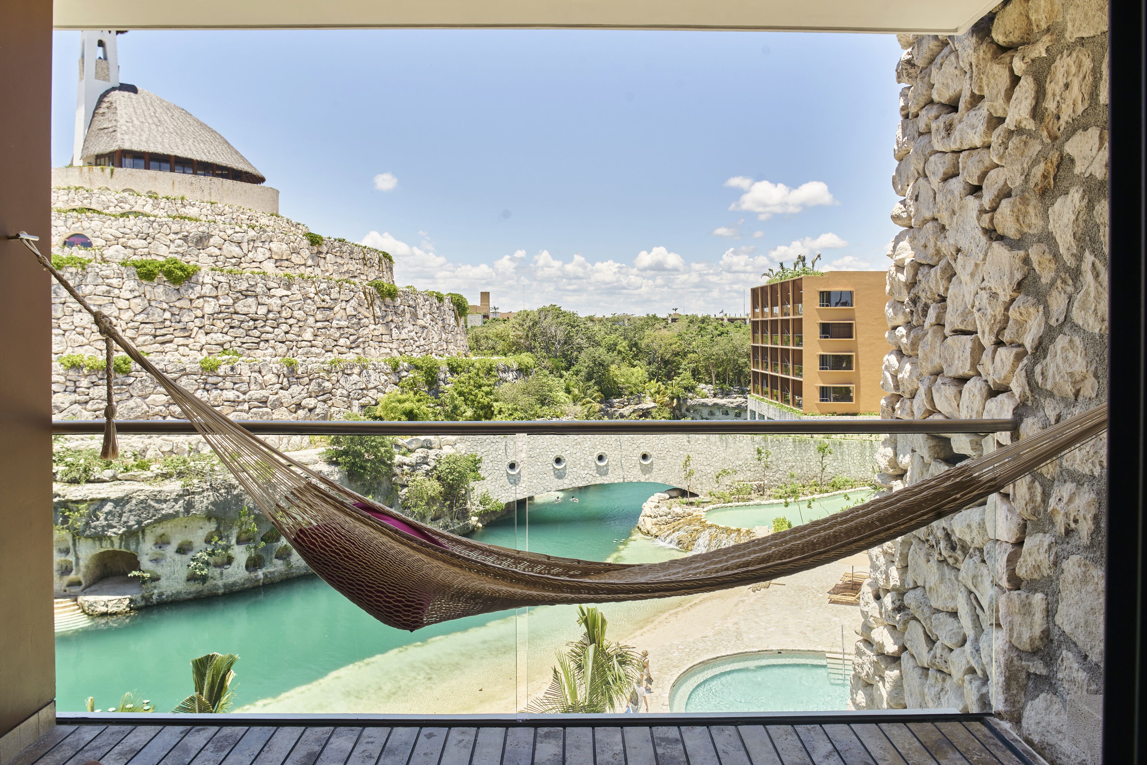 Una hamaca en un balcón con vista a una piscina, un muro de piedra y un edificio con una cúpula.