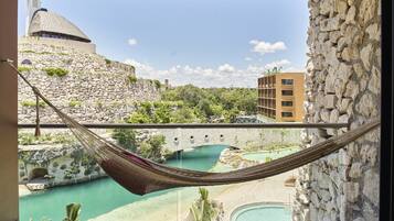 Una hamaca en un balcón con vista a una piscina, un muro de piedra y un edificio con una cúpula.