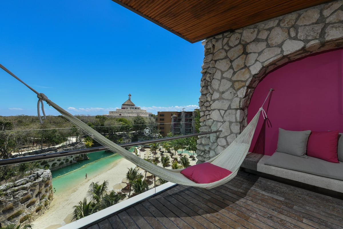 Una silla hamaca con un cojín rosa en un balcón con vistas a una playa y un edificio con cúpula.
