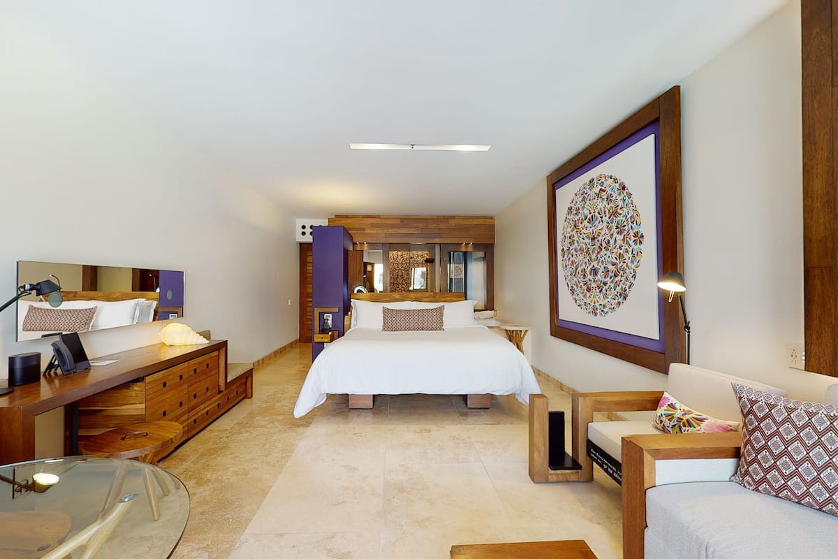 Una habitación de hotel moderna con una cama grande, un escritorio con lámpara, una silla, un sofá y una mesa de vidrio.