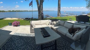 En terrasse med en fletsofa, et bord og en grill, med udsigt over en sø med en anløbsbro og både.