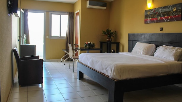 A hotel room with a bed, a desk, a chair, a potted plant, and a painting on the wall. - Residence Les Hauts de L Indenie (Abidjan)