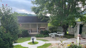 Un espace patio agrémenté d’un chemin de pierre menant à un coin salon avec une table et des chaises, le tout entouré d’une végétation luxuriante et d’une structure en forme de pergola.