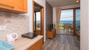 A kitchen with a coffee maker, a microwave, and a blue tray. There is a wooden cabinet and a countertop. The room has a view of the ocean through a glass door. - Arabela 2 Apartments (Utjeha)