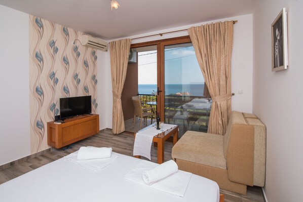 A hotel room with a TV, two beds, a balcony with a table and chairs, and a view of the sea. - Arabela 2 Apartments (Utjeha)
