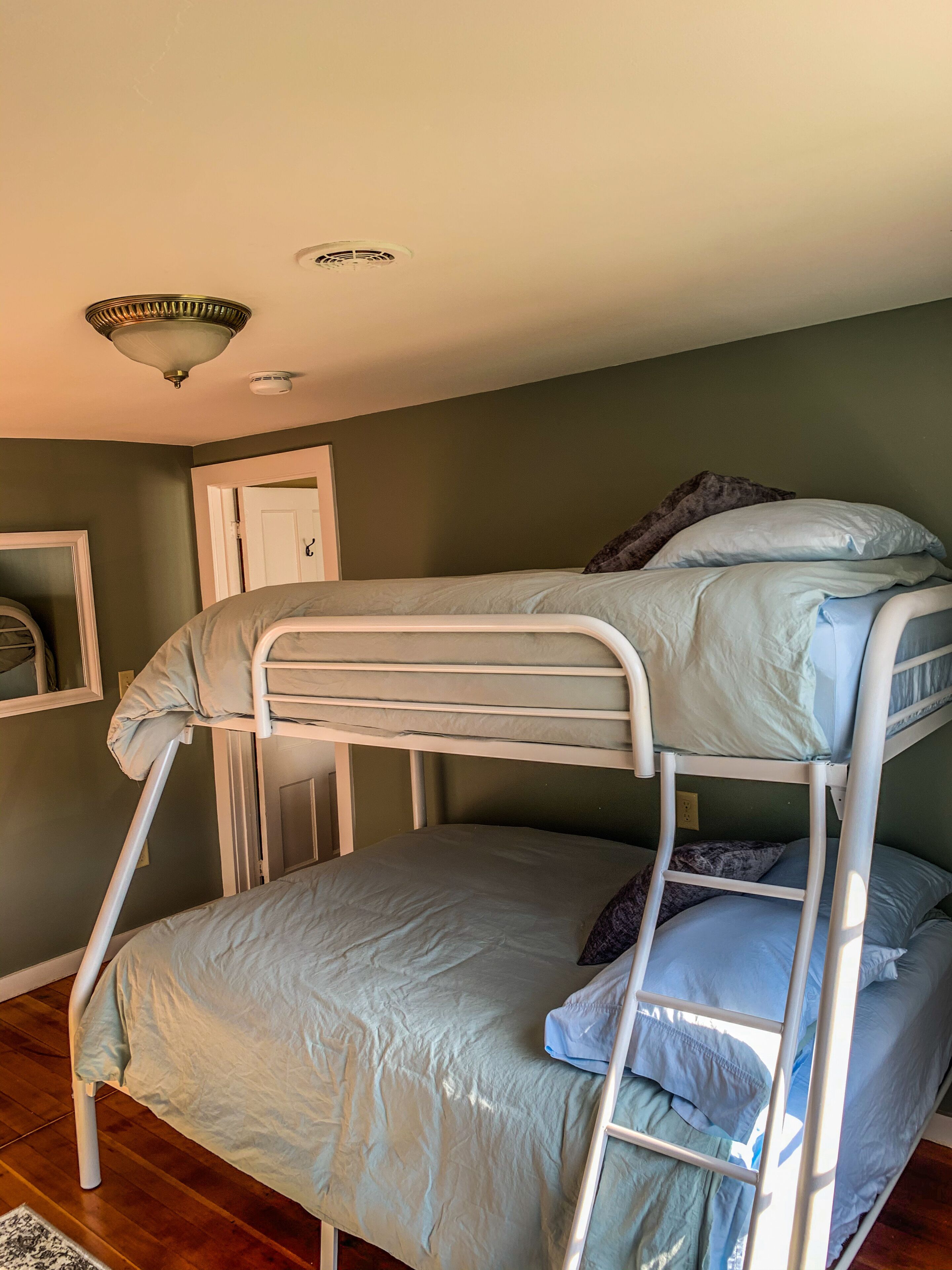 Ein Etagenbett in einem Zimmer mit grünen Wänden, einer weißen Tür und einer Deckenleuchte.