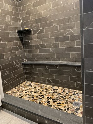 A shower area with dark marble tiles and a pebble-patterned floor. - Comfy Cottage with Private Hot Tub in Historic East Poultney (Poultney)
