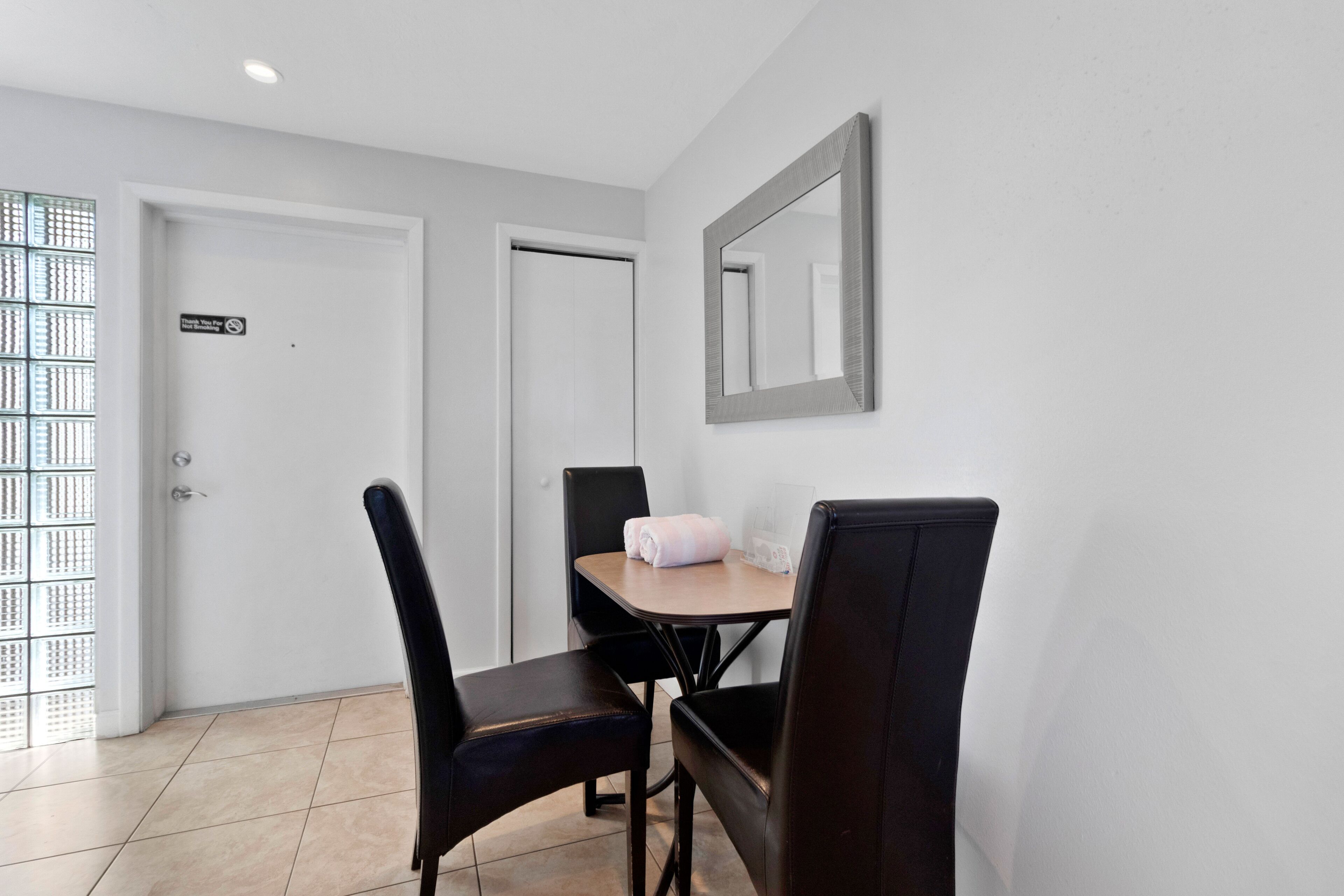 A small dining area with a table and four chairs, a mirror on the wall, and a door with a sign.