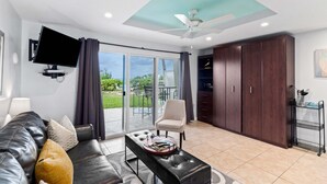 Un salon moderne comprenant un canapé, une table basse, un téléviseur fixé au mur, un ventilateur de plafond et une porte-fenêtre coulissante donnant sur un espace extérieur.