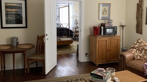 Ein Wohnzimmer mit Couchtisch aus Holz, einem blumengemusterten Sessel, einem braunen Sofa, einem Schrank und einer Tür zu einem anderen Raum.