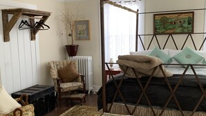 Ein Schlafzimmer mit einem Himmelbett, einem Sessel, einem kleinen Tisch und einem großen Teppich.