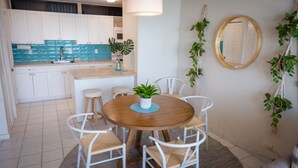 A dining area with a round wooden table, white chairs, and a potted plant in the center. - Ocean View, Spacious Condo next to Pool (St Thomas)