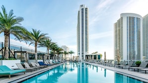 Une piscine entourée d’immeubles imposants, avec des chaises longues et des palmiers.