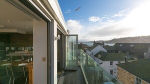 A balcony with a glass door leading to a dining area, overlooking a coastal town.