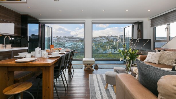 A modern kitchen with a dining area, large windows, and a view of a cityscape.