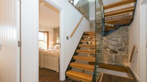 A modern staircase with glass railings and wooden steps leading to a stone wall.