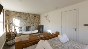 A bedroom with a stone wall, a wooden bedside table, a bed with floral bedding, and a white door.