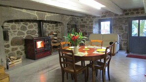 A cozy dining area with a stone fireplace, wooden chairs, a table set for four, and a sofa in the background. - Country home (Montboudif)