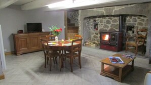 A cozy living room with a stone fireplace, wooden furniture, and a television. - Country home (Montboudif)