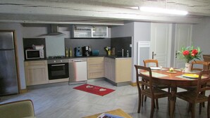 A compact kitchen with modern appliances, a dining area with a wooden table and chairs, and a red rug on the floor. - Country home (Montboudif)