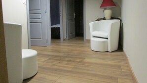 A room with a white chair, a red lamp, and a bed in the background. - Country home (Montboudif)
