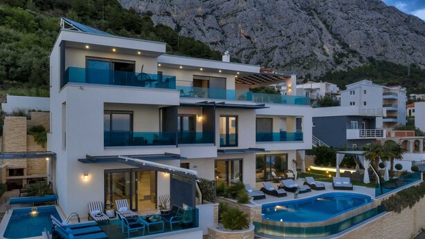 Une villa moderne à plusieurs étages, dotée d’une piscine, d’un espace salon extérieur et offrant une vue sur les montagnes.