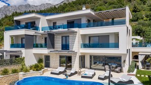 Une villa moderne à deux étages, dotée d’une piscine, d’un espace salon extérieur et offrant une vue sur les montagnes.