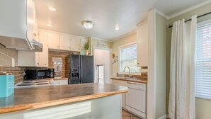 A modern kitchen with white cabinets, a black refrigerator, a wooden countertop, and a window with white curtains. - Kimball Cottage (Richland)