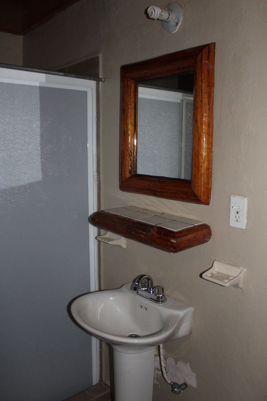 Une salle de bain avec un lavabo blanc, une étagère en bois au-dessus, et un miroir avec un cadre en bois.