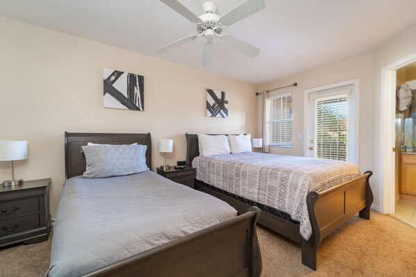 A bedroom with two beds, a ceiling fan, and artwork on the walls.