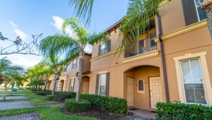 A row of townhouses with a brick pathway, palm trees, and a clear blue sky. - Regal Palms Resort  Communal Pool, Arcade, Fitness Center & Tennis (Davenport)