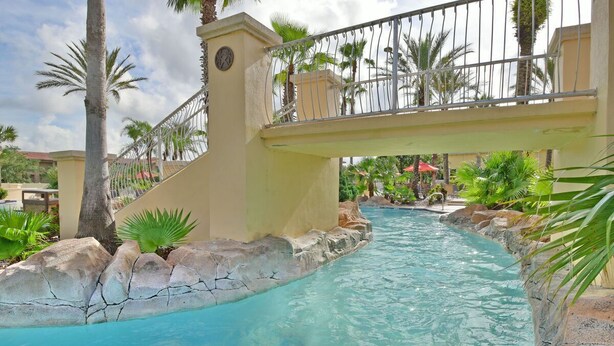 A pool area with a bridge, palm trees, and a stone border. - Regal Palms Resort  Communal Pool, Arcade, Fitness Center & Tennis (Davenport)
