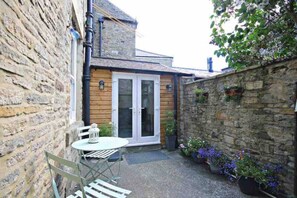 A small, enclosed patio area with a table and chairs, a door leading to a covered space, and a stone wall with potted plants. - Charming 2-bed Cottage in the Heart of Stanhope (Bishop Auckland)