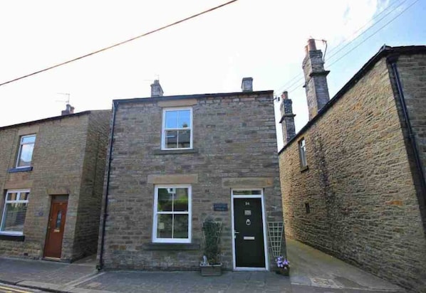 A two-story stone building with a black door and a small window. - Charming 2-bed Cottage in the Heart of Stanhope (Bishop Auckland)