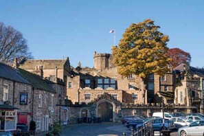 A historic stone building with a central archway, surrounded by parked cars and a clear sky. - Charming 2-bed Cottage in the Heart of Stanhope (Bishop Auckland)