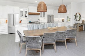 Una cocina moderna con armarios blancos, electrodomésticos de acero inoxidable, una mesa de comedor de madera y sillas de mimbre.