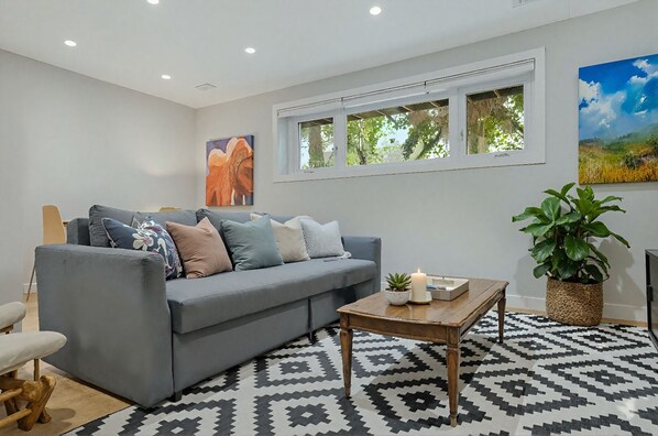 A modern living room with a grey sofa, patterned rug, and a large window with a view of greenery.