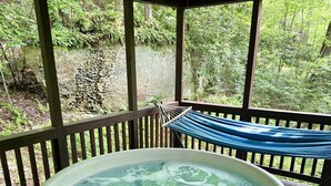 Een hottub op een houten terras, met een hangmat en uitzicht op een bebost gebied.