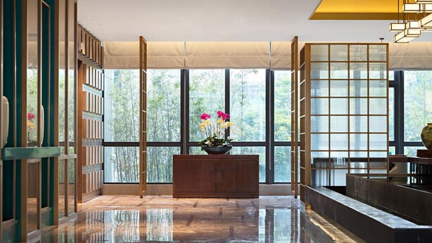 A spacious lobby with a polished floor, large windows offering a view of greenery, a wooden reception desk, and a traditional-style partition with sliding doors. - Tangyi Hotel Zhuhai (Zhuhai)