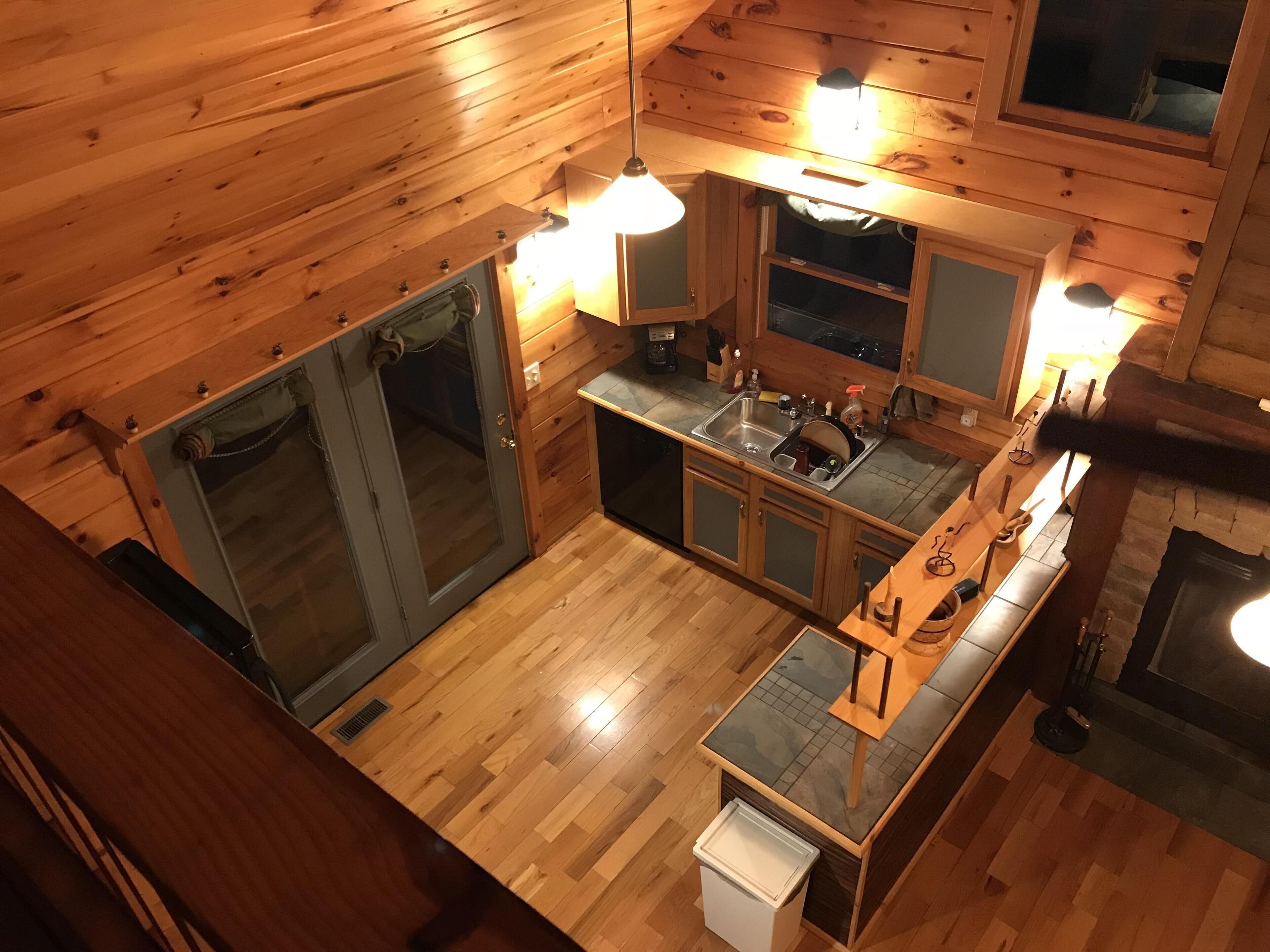 A wooden cabin interior with a kitchen area, including a sink, cabinets, and a small trash bin.