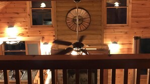 A wooden interior with a sloped ceiling, a ceiling fan, and a clock on the wall. - Cabin at Scenic Heights with a hot tub and wi-fi (Campton)