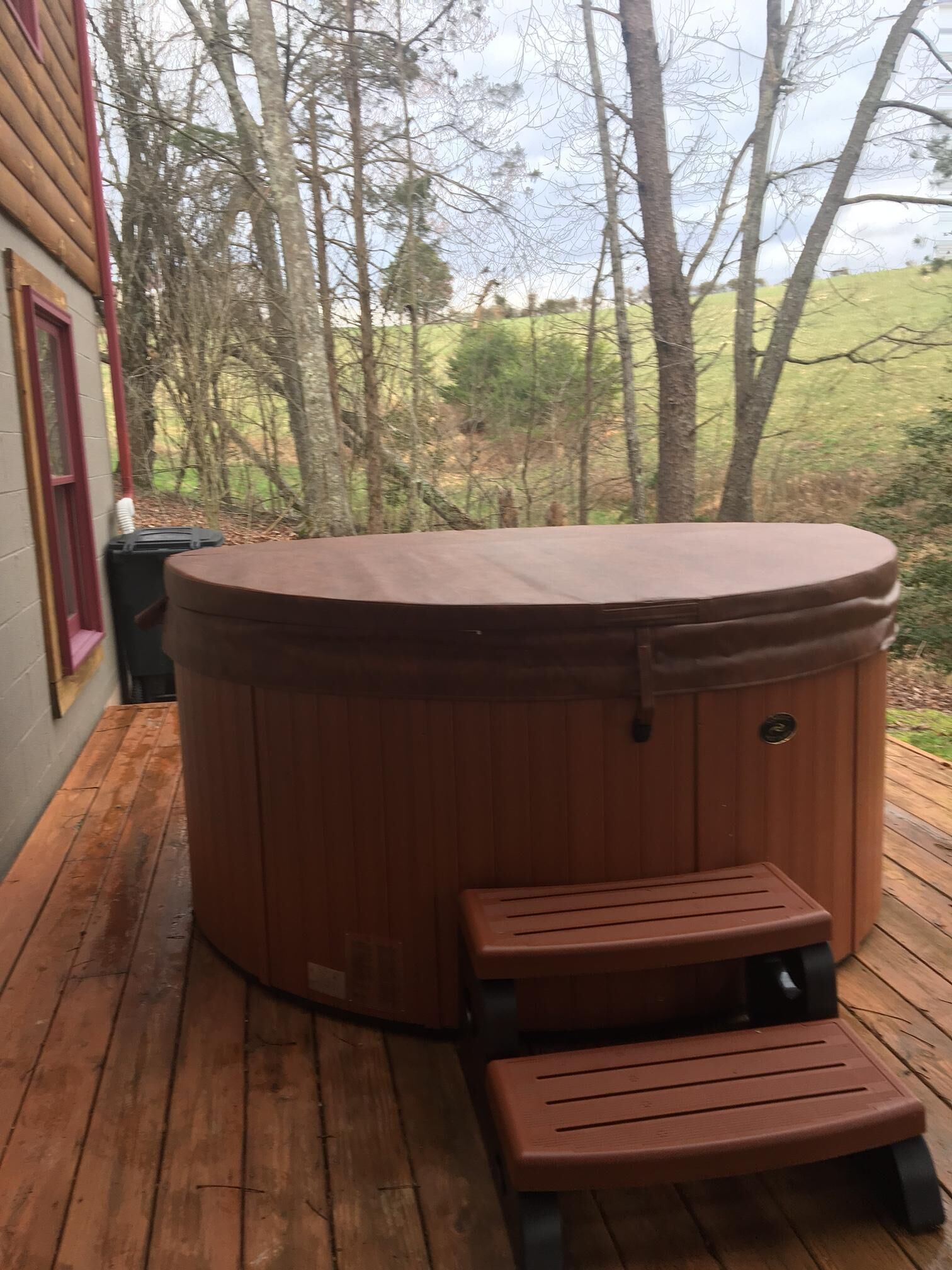 A hot tub with a wooden deck, a small bench, and a window with a red frame.